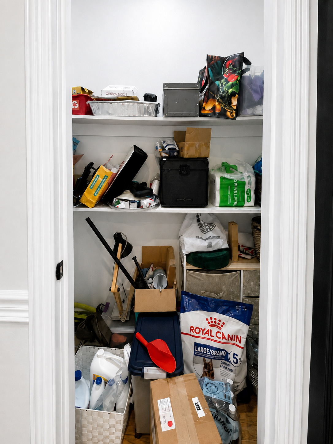 Pantry closet before organizing, with mixed household items stacked on shelves and the floor