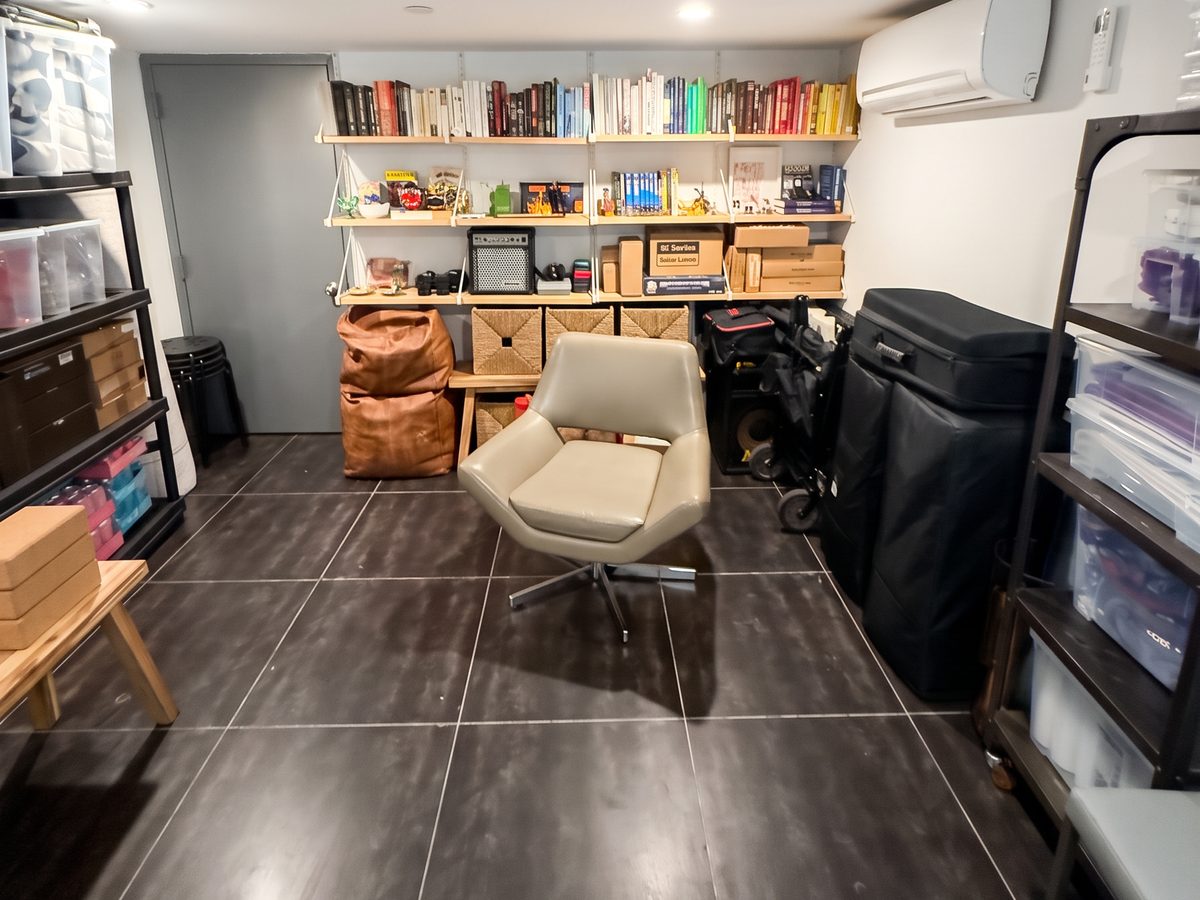 Basement after organizing, with color-sorted books on open shelving, woven baskets and a lounge chair