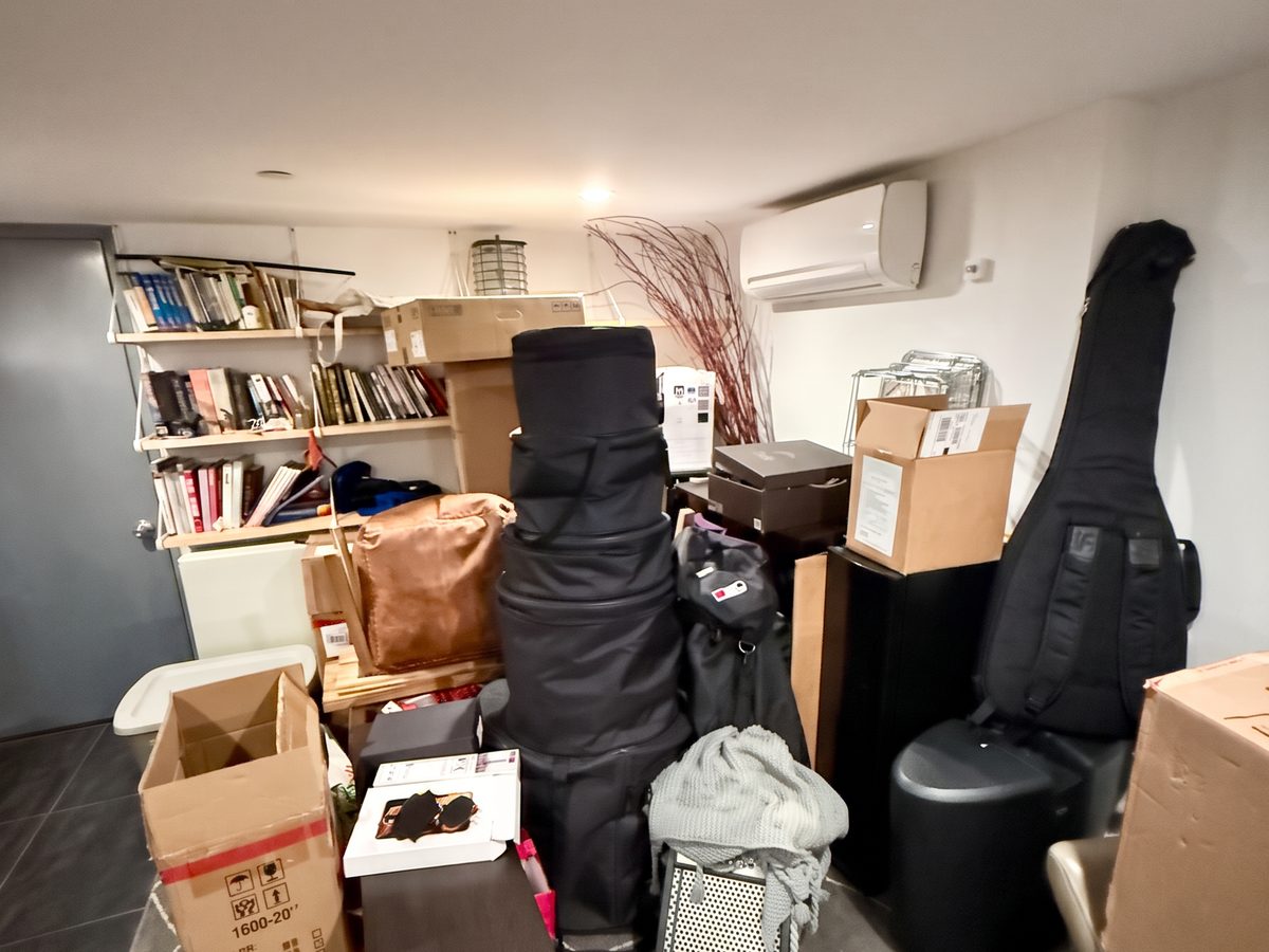 Basement corner before organizing, with instrument cases, bags and boxes stacked on the rug